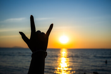 silhouetted hand making the "I Love You" sign in front of a radiant sunset over the ocean