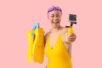 Female African-American swimmer with flippers taking video on pink background