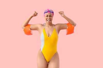 Happy female African-American swimmer with inflatable armbands on pink background