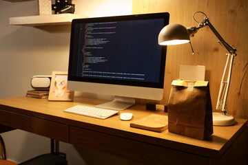 Paper bag with glowing lamp and computer on desk in office at night. Food delivery service