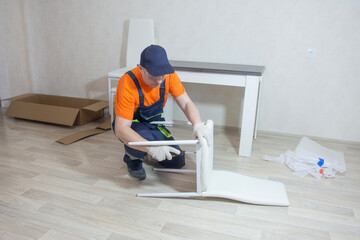 A middle-aged man in a special jumpsuit is assembling a chair from parts in a bright room