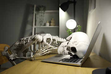 Human skeleton model lying on laptop in office at night