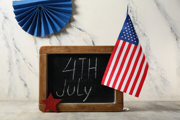Chalkboard with text 4TH JULY and USA flag on table against white marble background. Independence...