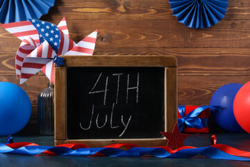Chalkboard with text 4TH JULY and ribbons on table against wooden background. Independence Day...