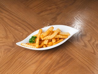 Crinkle cut French fries served on a white plate over wooden table