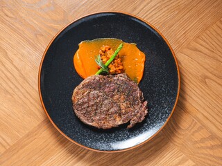 Grilled ribeye steak with sweet pepper sauce and asparagus on black ceramic plate