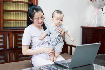 Mother interacts with baby while using laptop for virtual session in cozy living room during daytime