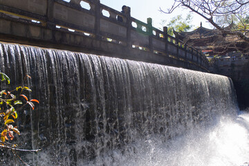 waterfall flowing beneath ancient stone bridge in scenic garden