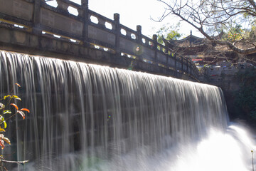 waterfall flowing beneath ancient stone bridge in scenic garden