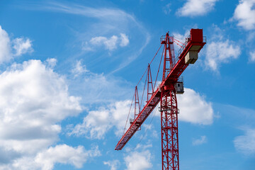 A striking red construction crane set against a vibrant blue sky dotted with fluffy white clouds, symbolizing industrial progress and urban development.