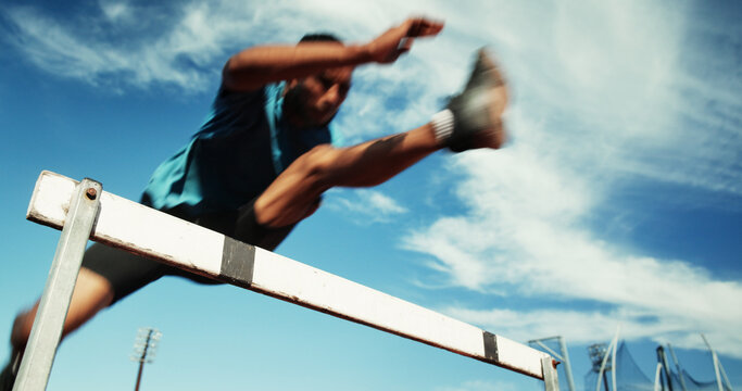 Man, athlete and jump by hurdle for fitness competition, challenge and contest at sports field. Low angle, sprint obstacle and sky with blur for speed, leap and performance for marathon event