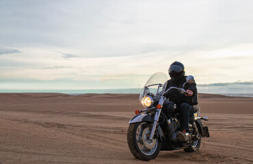 Obraz premium Man on motorcycle in desert during sunset with dramatic clouds — concept of freedom, travel, solitude, adventure, and outdoor lifestyle in wild open landscapes