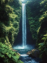 Tall narrow waterfall cascading into a pool surrounded by dense lush green tropical plants and trees under soft natural light