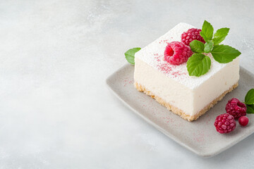 Piece of cheesecake with fresh raspberries and mint on a plate on a light background, copy space. Summer dessert