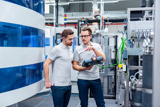 Two employees discussing in a production hall with machinery