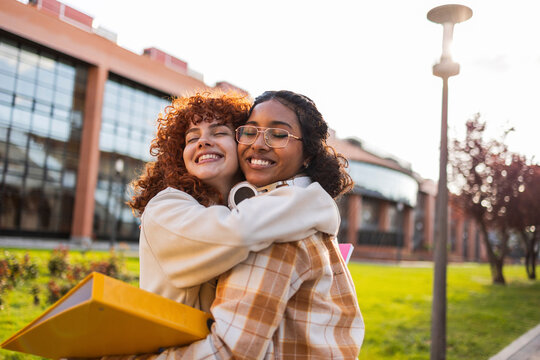 Two students smiling and hugging on a university campus outdoors