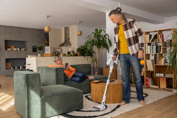 Man vacuuming while woman relaxes in modern living room