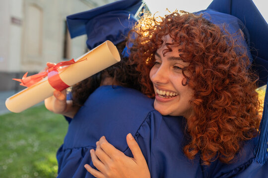 University students in blue gowns celebrating graduation with a joyful hug outdoors