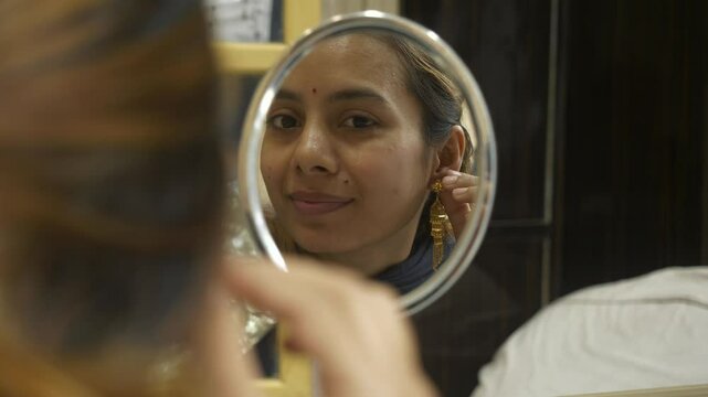 Young beautiful asian woman looking at mirror wearing 18k HUID certified gold earrings