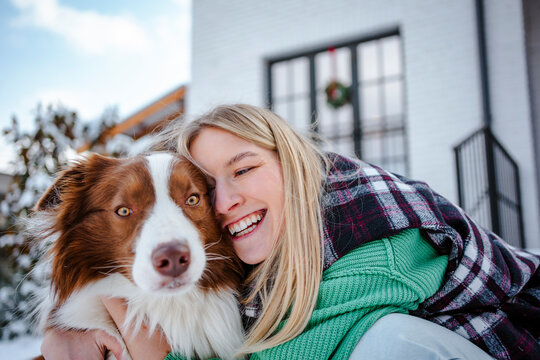 Blond woman smiling with her dog in a snowy backyard
