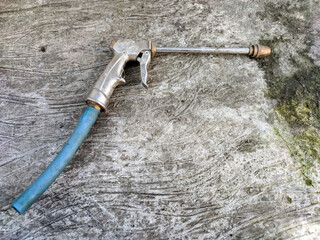 A robust, metallic spray gun, possibly an attachment for a pressure washer or air compressor, featuring a long nozzle and a light blue hose connection, resting on a rough.