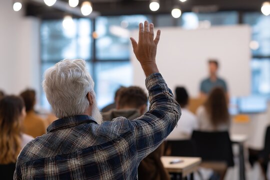 Back view of older student raising his hand to answer teacher's question during education training class. High quality