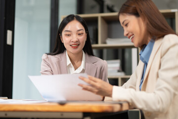Two professional business executives working on laptop computer sitting at office desk, happy colleagues discussing company digital strategy.