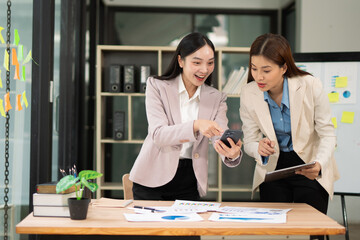 Two excited Asian businesswomen raising their arms and delighted at a successful company event in an office environment.