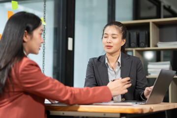 Group of happy Asian business people having a meeting at the office. Two women working together using modern laptops.