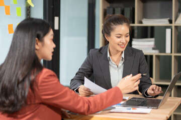 Two professional business executives working on laptop computer sitting at office desk, happy colleagues discussing company digital strategy.
