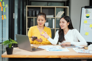 Obraz premium Two professional business executives working on laptop computer sitting at office desk, happy colleagues discussing company digital strategy.