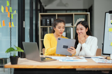 Two excited Asian businesswomen raising their arms and delighted at a successful company event in an office environment.