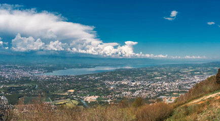 Vue panoramique spectaculaire du bassin genevois depuis le Salève, révélant la ville de Genève, le lac Léman et les montagnes environnantes sous une lumière naturelle et dégagée.
