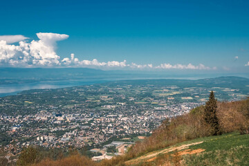 Vue panoramique spectaculaire du bassin genevois depuis le Salève, révélant la ville de Genève, le lac Léman et les montagnes environnantes sous une lumière naturelle et dégagée.