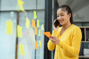 Two Asian businesswomen brainstorming using sticky notes in an office.