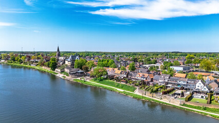 Aerial drone view of typical Dutch village, idyllic countryside landscape with traditional houses and church near river Meuse in spring, Limburg province, the Netherlands