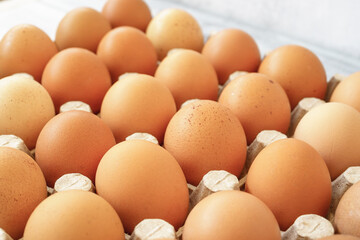 Brown chicken eggs in a cardboard tray on a rustic wood background for farm and food concepts and healthy eating or cooking recipes and ingredients advertising.