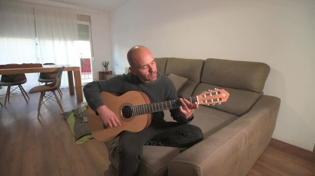 Musician playing acoustic guitar at home on sofa