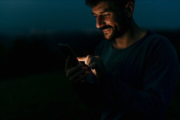 Smiling man using smartphone at night in nature