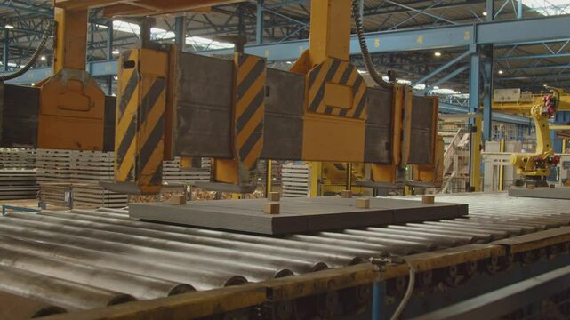 A crane moves over a stack of steel plates on a roller bench