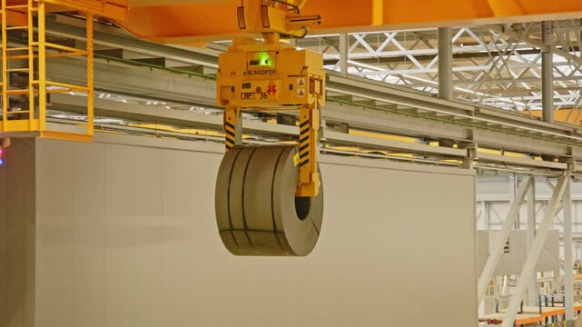 Close up of a overhead bridge crane moving a heavy steel coil in an automated warehouse
