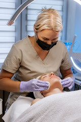 Fototapeta premium Close-up of professional esthetician performing a facial treatment with cotton pad on woman’s neck during beauty session at a spa, skincare procedure 