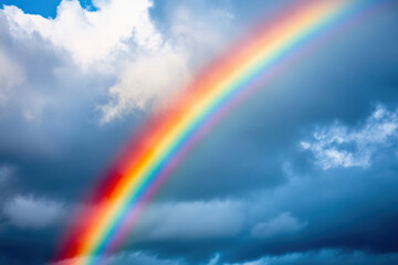 Rainbow shining brightly in the blue sky with clouds and summer light