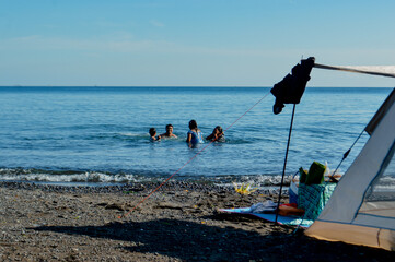 The four family members wade and enjoy the calm sea water while camping near the beach.