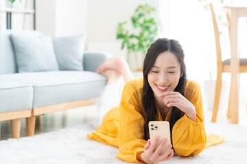 リビングでスマホを見ながらくつろぐ若い女性
