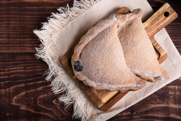 Close-up of two delicious empanadas dusted with sugar, resting on a rustic wooden board