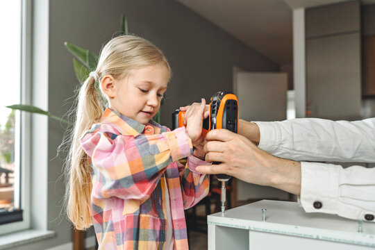 Father and daughter assembling furniture together at home using a drill