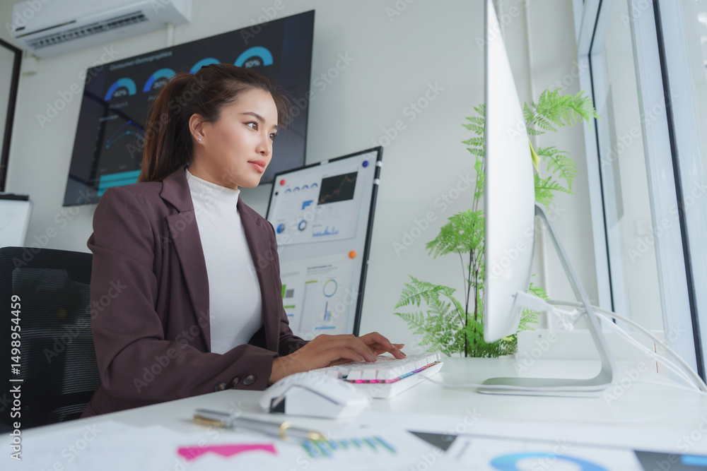 Poster businesswoman working at computer with charts and graphs displayed on screen and wall