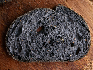 Fresh baked black charcoal sourdough ciabatta bread sliced on wooden board.