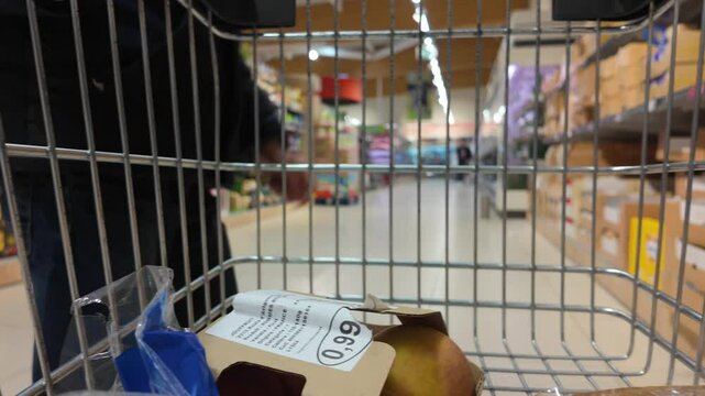 Metal shopping cart carrying fresh produce, cheese, water bottle, gliding through grocery store, capturing shopper's perspective while navigating market aisles